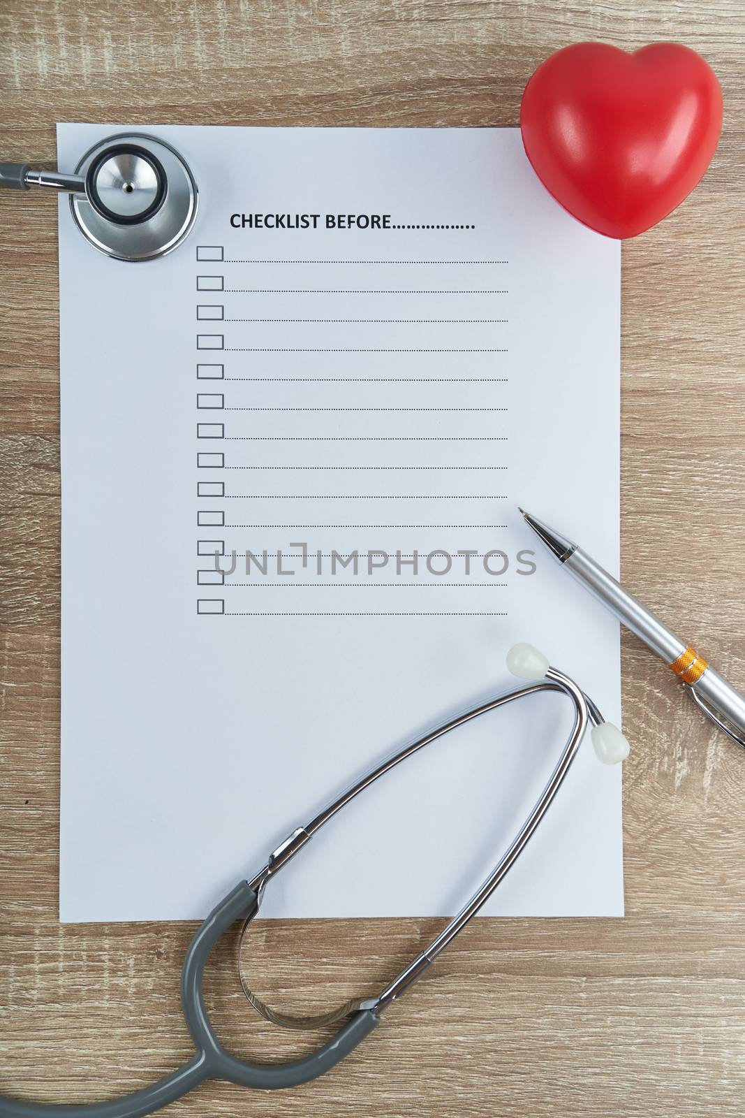 Close up old silver medical stethoscope and silver pen with red heart on empty checklist form with wood table and copy space. Healthcare and medical concept photography.
