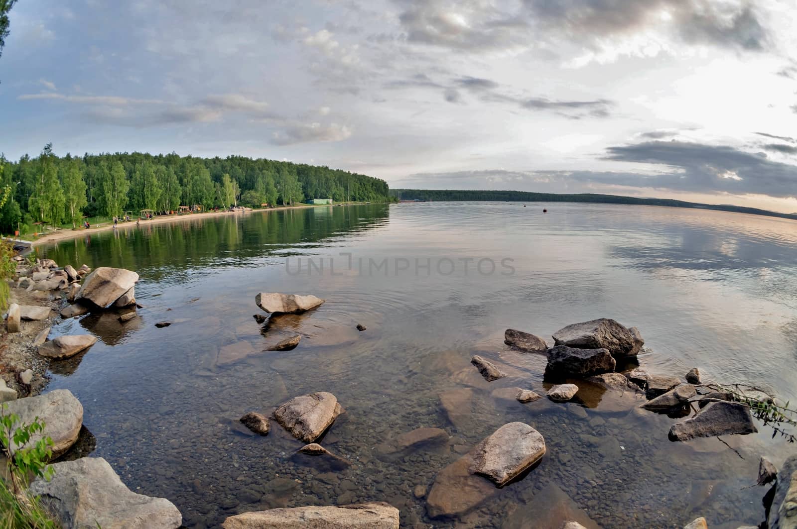 the evening sky over the lake, silhouettes of clouds illuminated by the sun, forest-covered, rocky shore of the lake