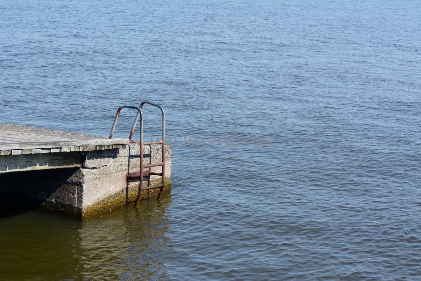 Rusted metal ladder on the side of a jetty, reaching down into water - with copy space
