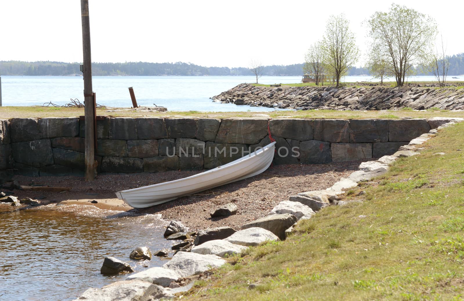 Small white rowboat on a small stony area of shore, against a stone wall on Suomenlinna island, Finland