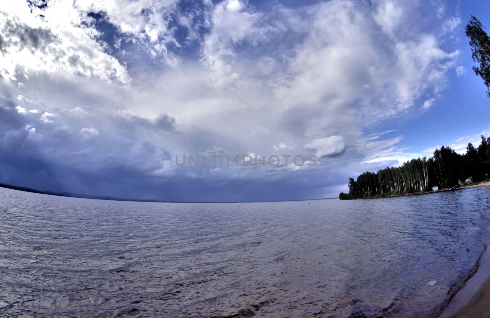 dark blue sky over the lake before the storm, the sun is shining
