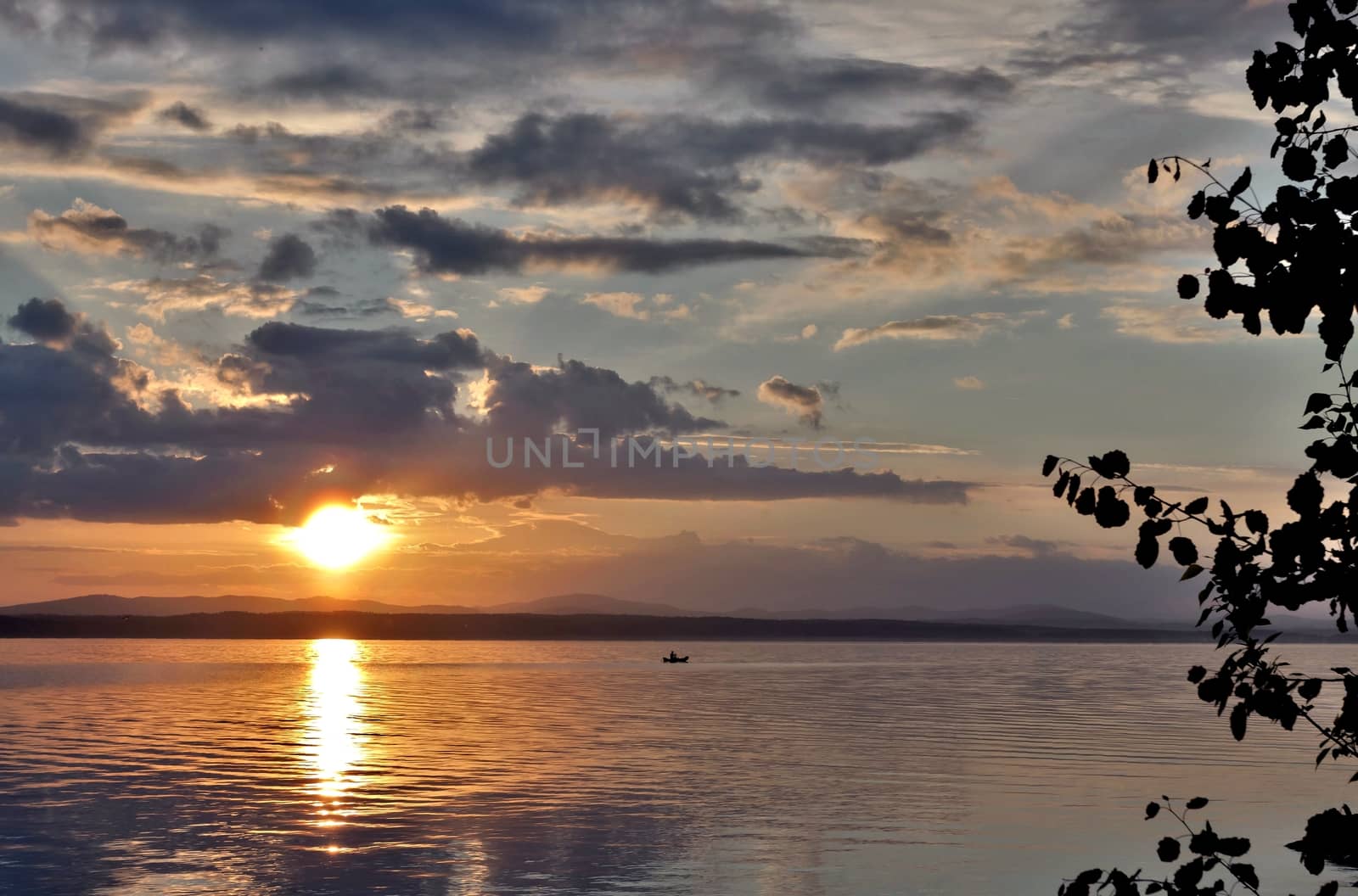 the evening sky over the lake, silhouettes of clouds illuminated by the sun, forest-covered shore of the lake