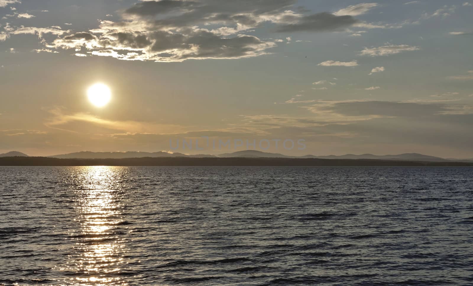 the evening sky over the lake, silhouettes of clouds illuminated by the sun