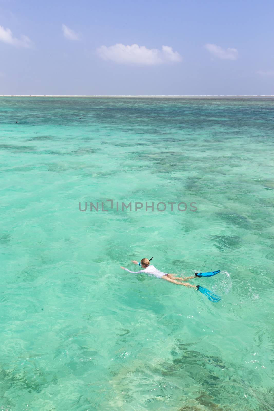 Woman snorkeling in clear shallow sea of tropical lagoon with turquoise blue water and coral reef, near exotic island. Mnemba island, Zanzibar, Tanzania.