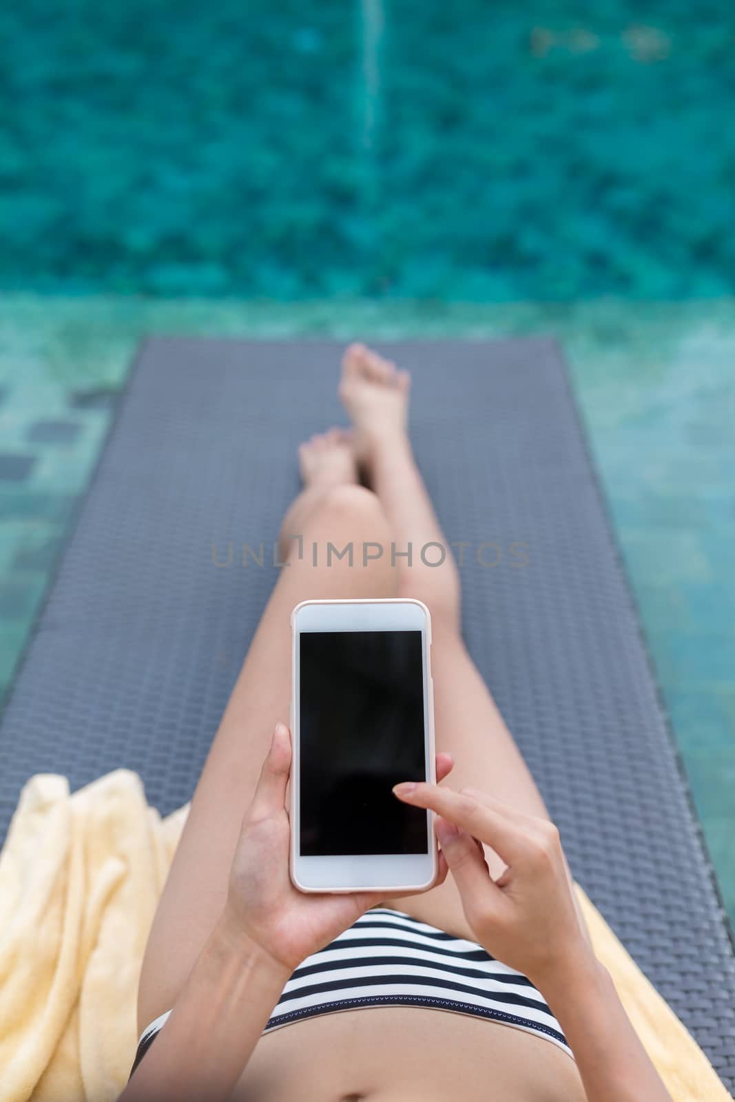 Woman relax on sunbath in swimming pool with using mobile phone by leungchopan