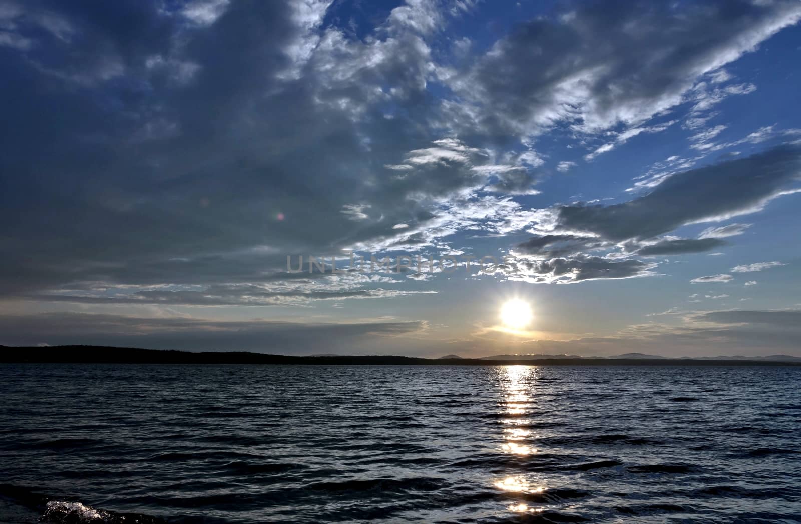 the evening sky over the lake, silhouettes of clouds illuminated by the sun