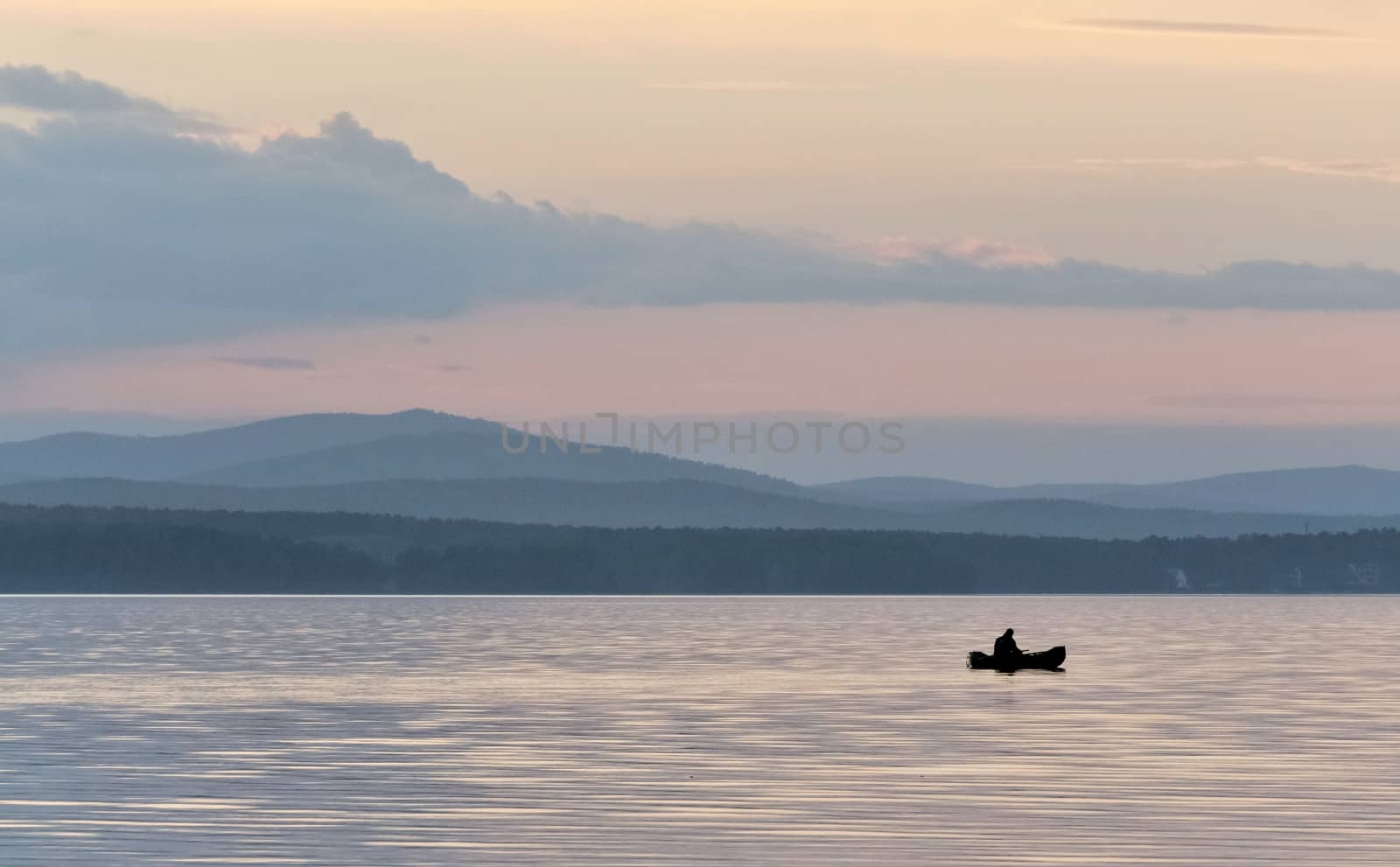 evening gray-blue lake and sky, a lone fisherman on a boat, in the distance you can see the silhouettes of the Ural mountains, the southern Urals, lake Uvildy