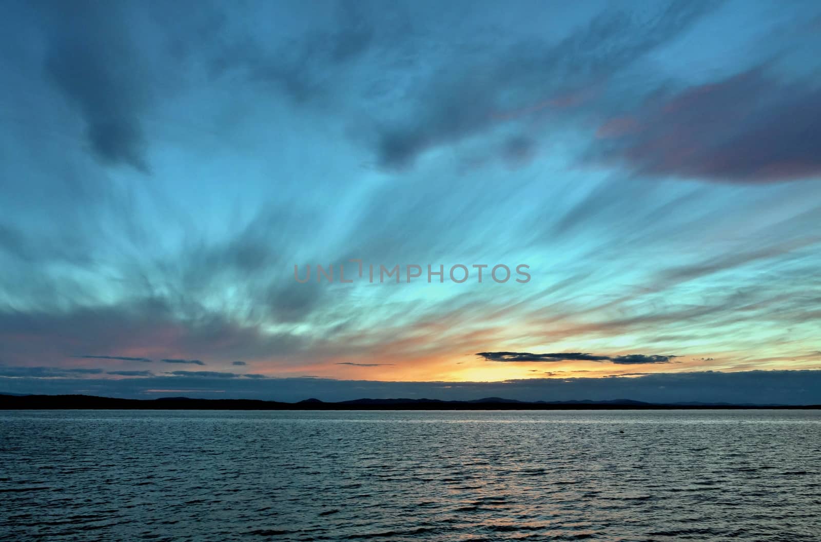 the evening sky over the lake, silhouettes of clouds illuminated by the sun, the sun sets over the horizon