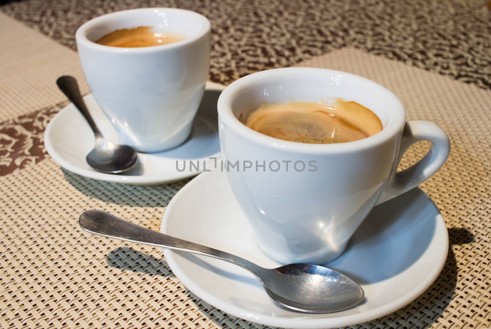 Composition of two cups of coffee on white serving plates with small metal spoons