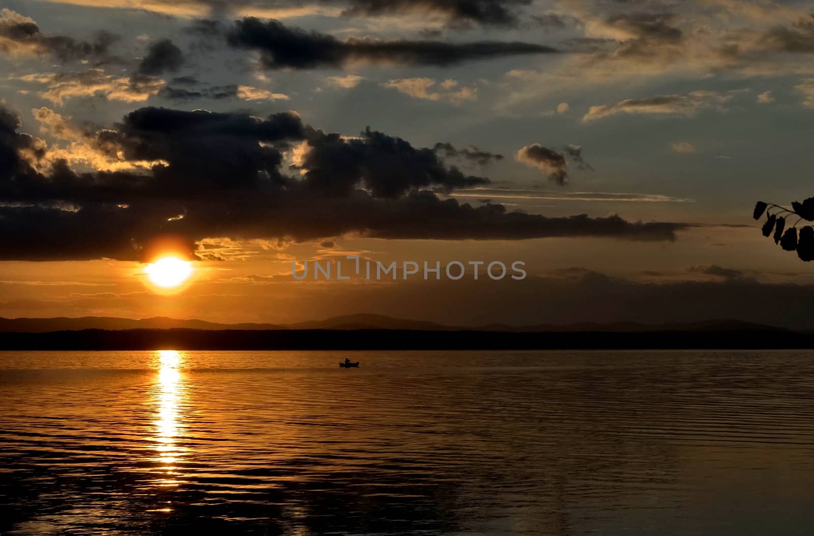 orange sunset over the lake, the sun lights up the clouds, a lone fisherman on a boat