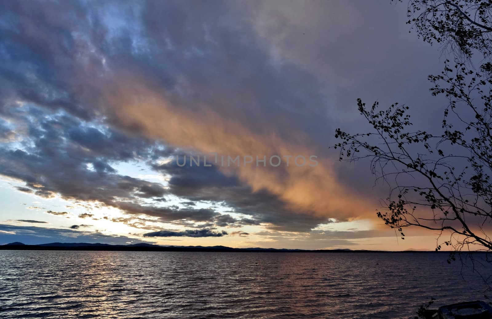 dark evening lake and orange sunlit clouds