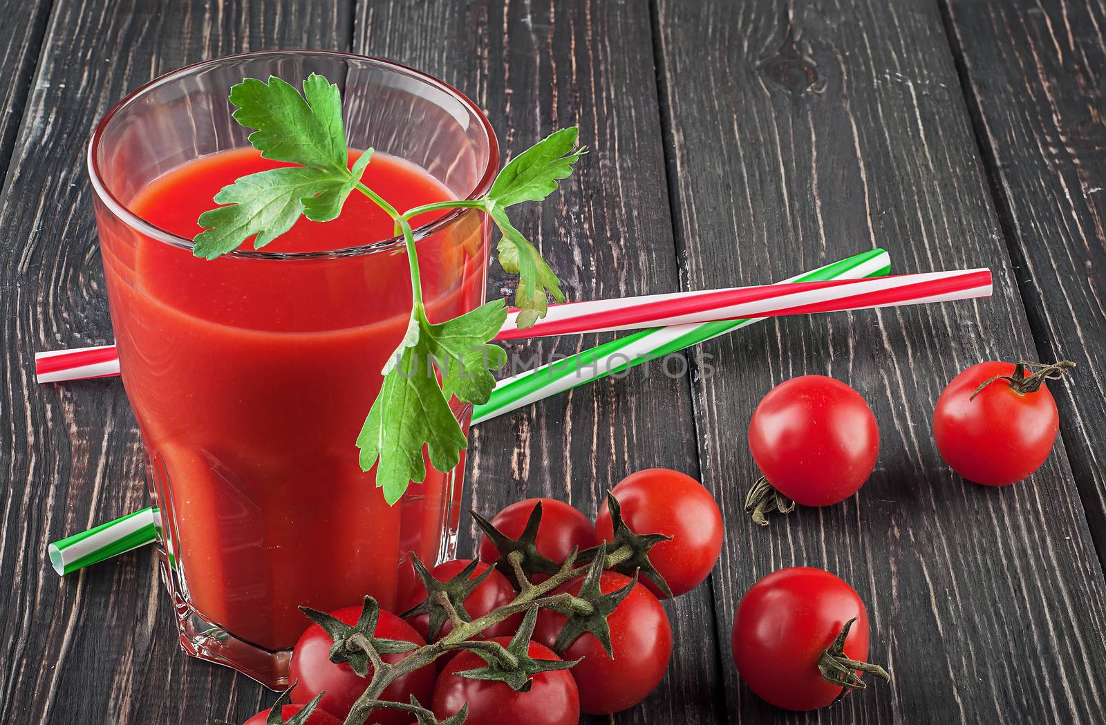Glass of tomato juice on wooden table. Cherry tomatoes and cocktail stick lying nearby.