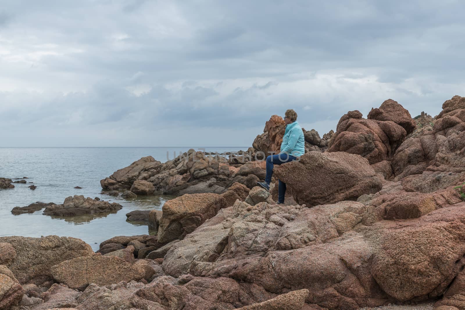 adult woman sitting on the rocks of isola rossa the read coast of sardinia island belongs to italy