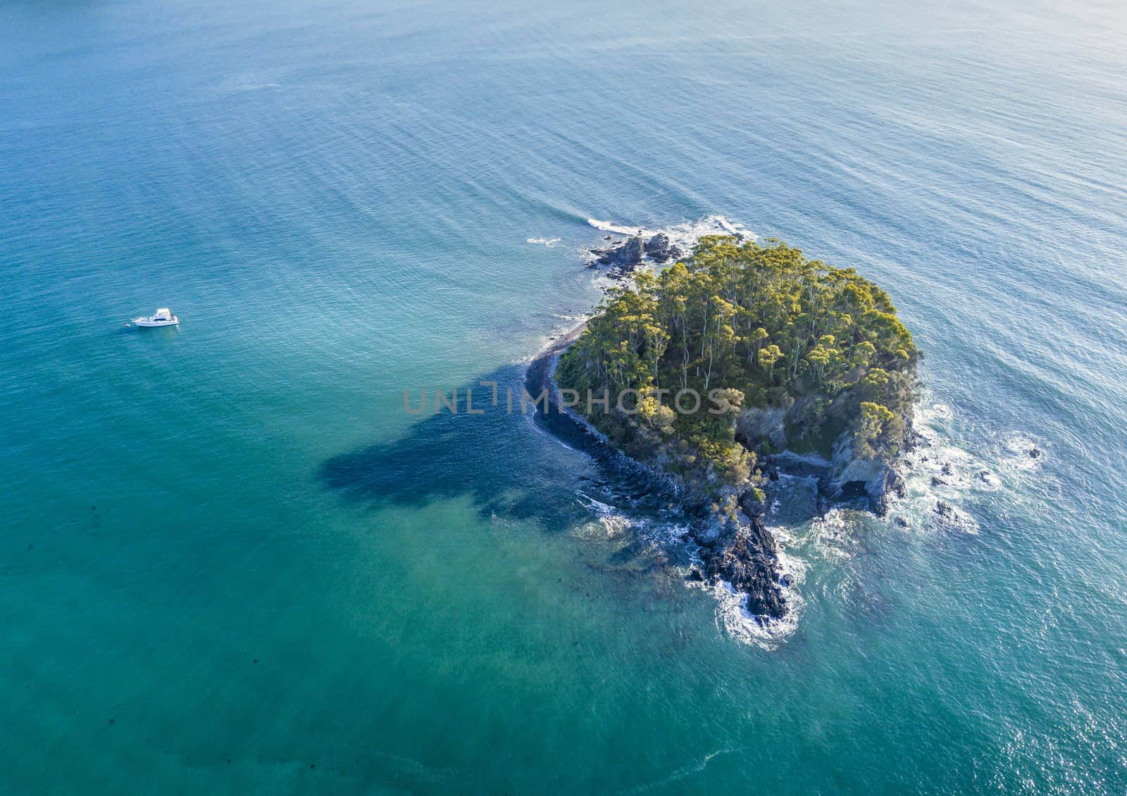 Aerial views of Snapper Island sitting 1 kilometre offshore in pristine aqua green waters of Batemans Bay Australia.  It lies a kilometre offshore and was a popular spot for smuggling as contraband could be hidden in the cave which had a back door escape route. Popular kayak or paddle venture.