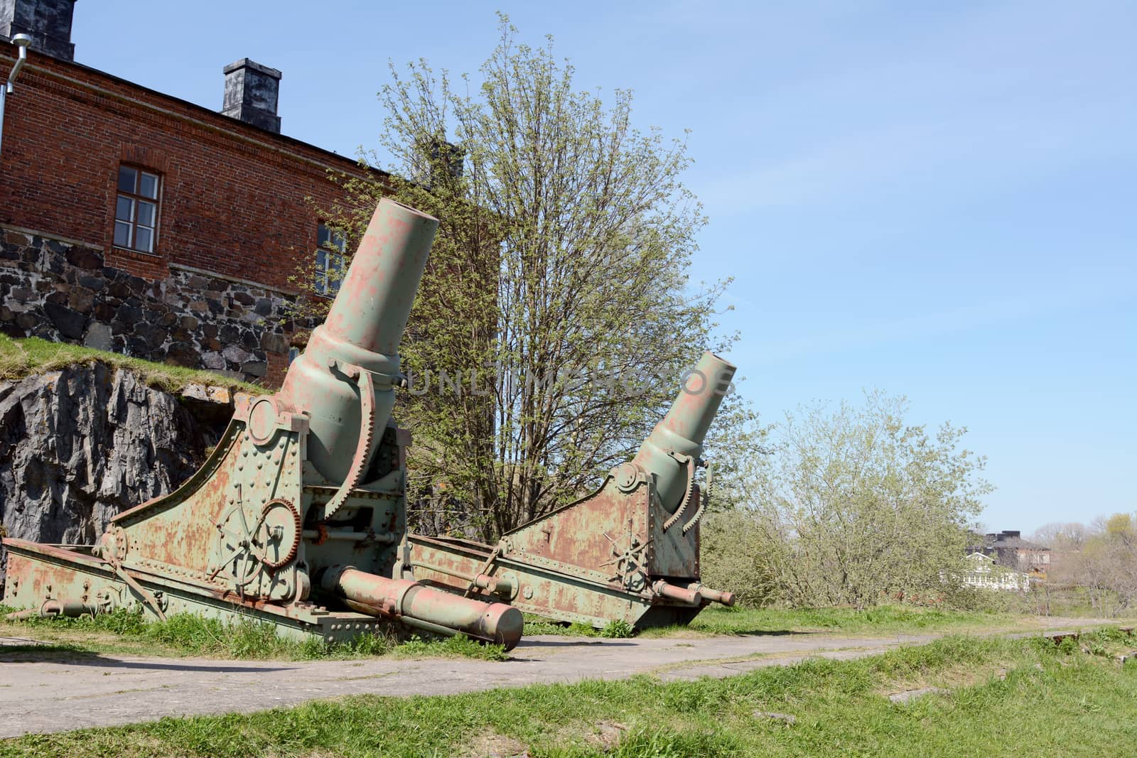 Two rusted green cannons in front of a military building on Suomenlinna island, Finland. A total of 100 stand on the sea fortress.
