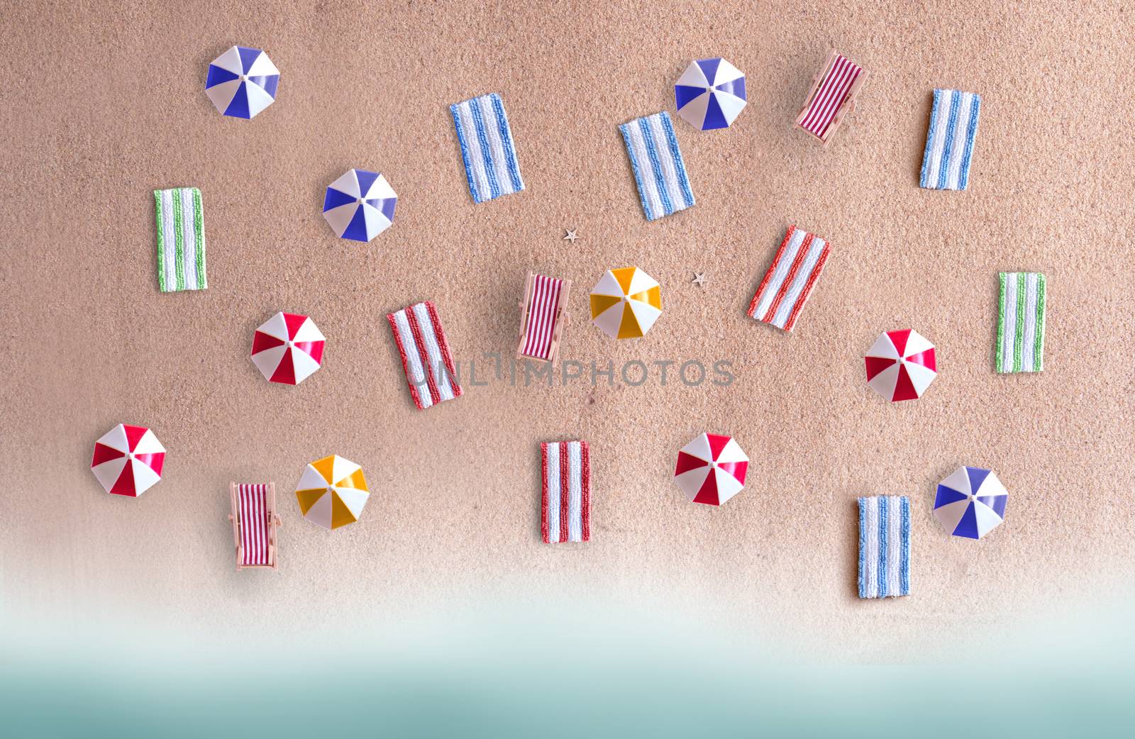 Miniature beach parasols and towels on sand 