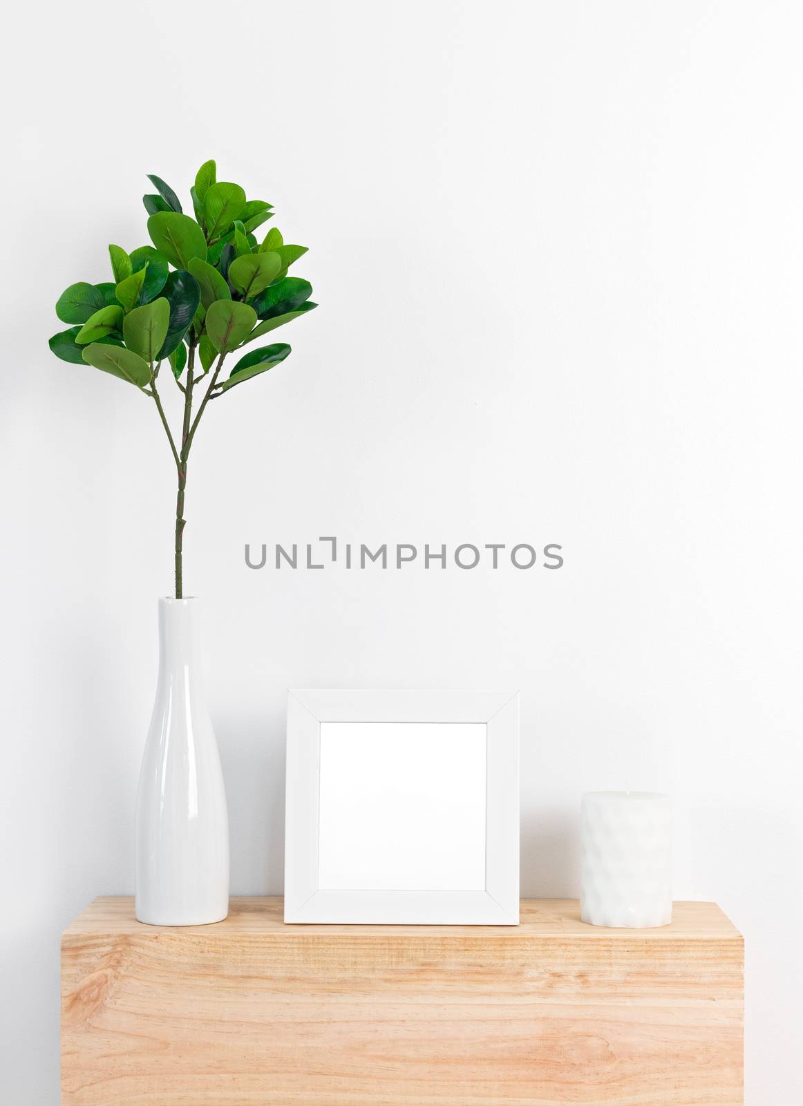 Stylish home decor with white picture frame, ficus leaves in a ceramic vase, and candle.