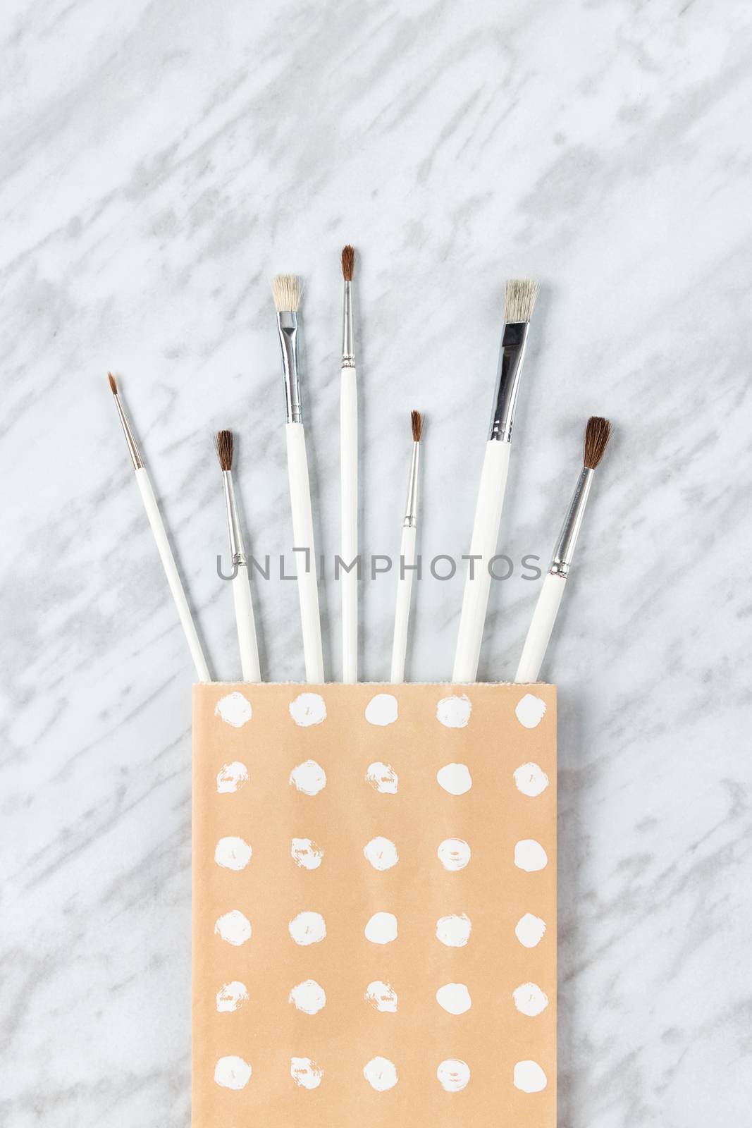 Paint brushes in a paper bag with white circles painted on it, on marble background.