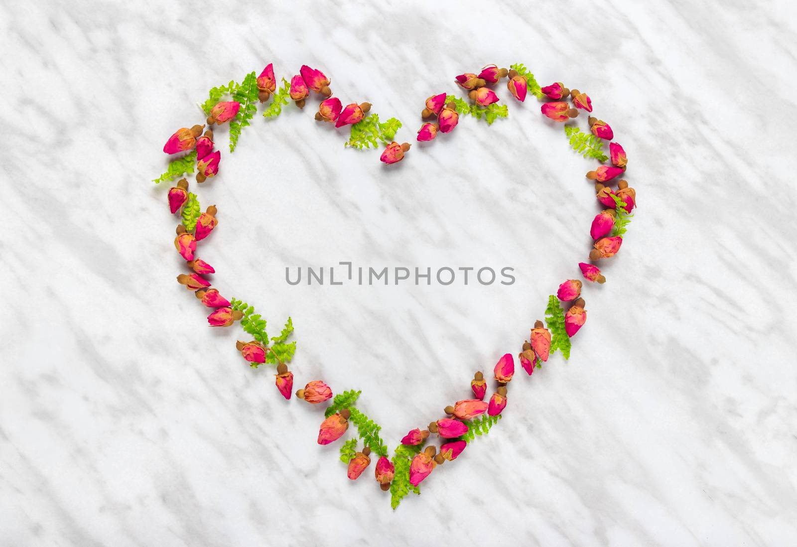 Heart made of rose buds and green leaves, on marble background.