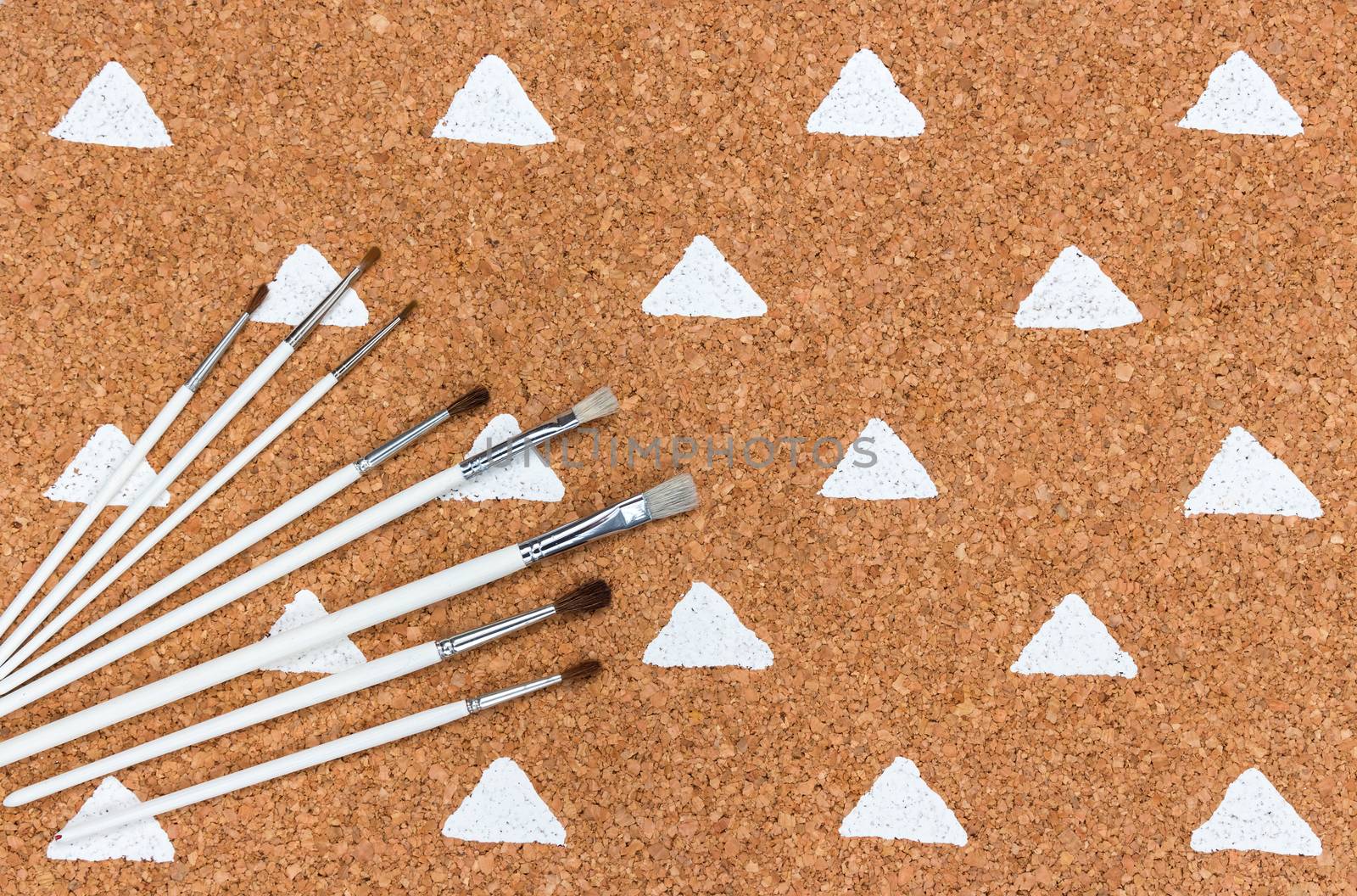 Paintbrushes on cork background simple design, white painted triangles.