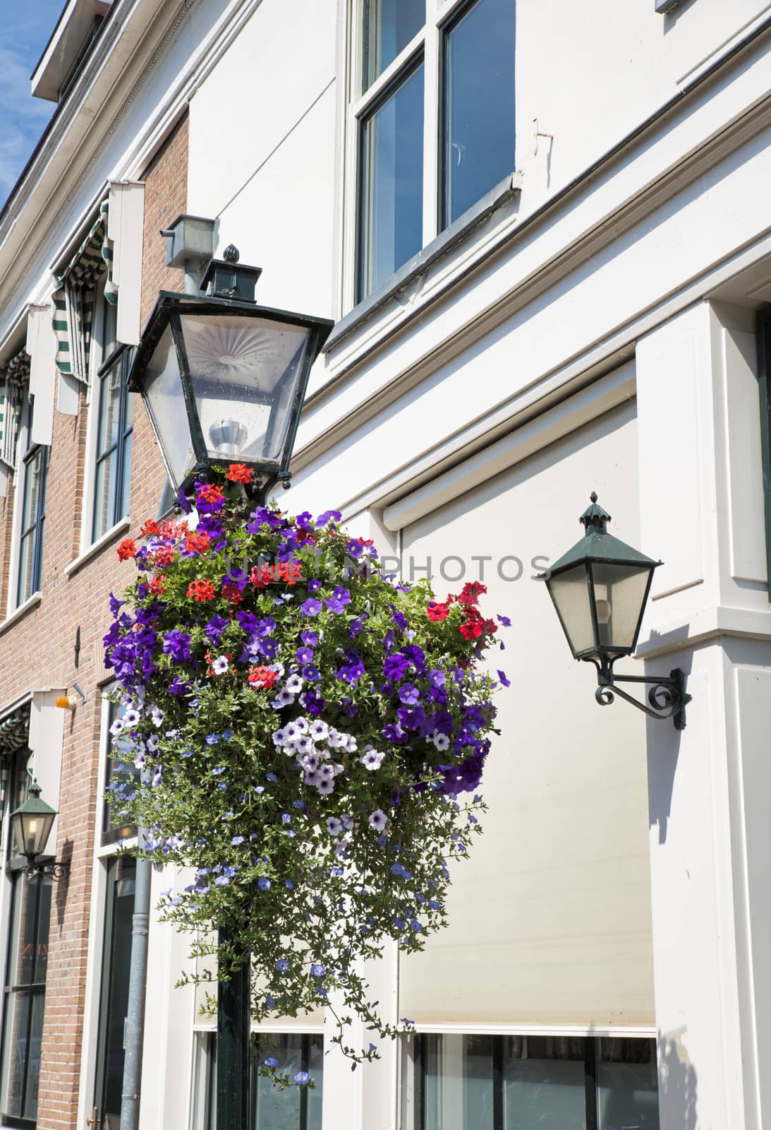 street with hanging basket full of flowers like geranium and petunias with old lights at the houses