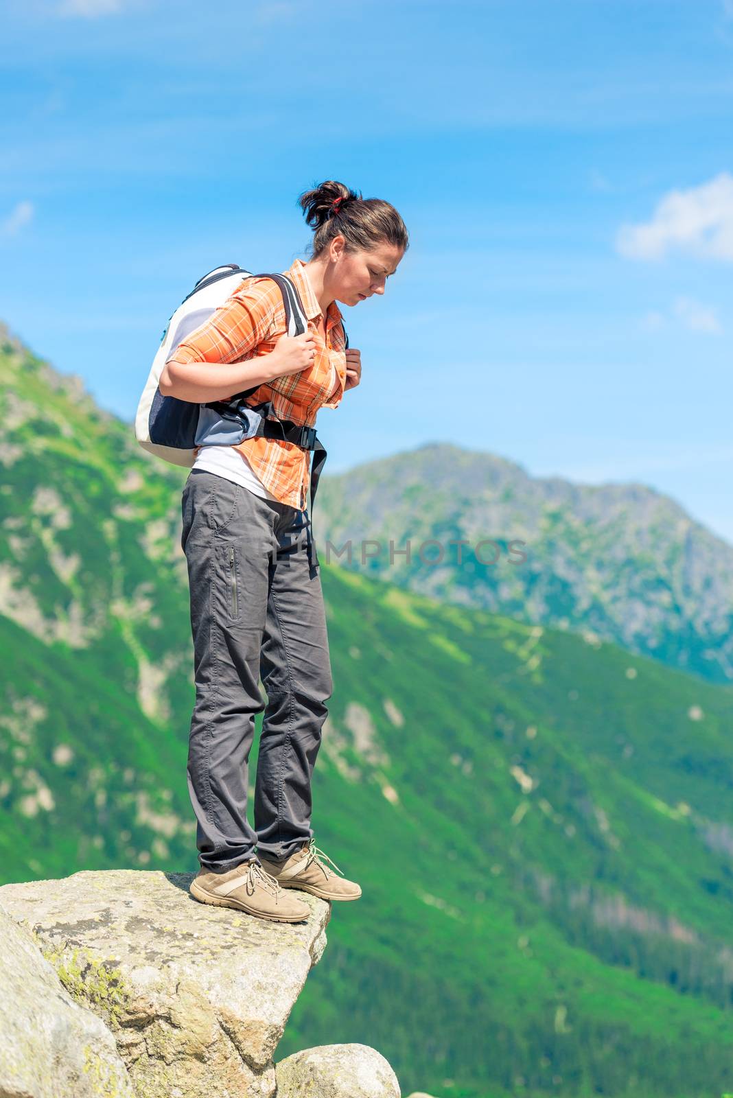 woman tourist with a backpack standing on a rock and looking down, dangerous route