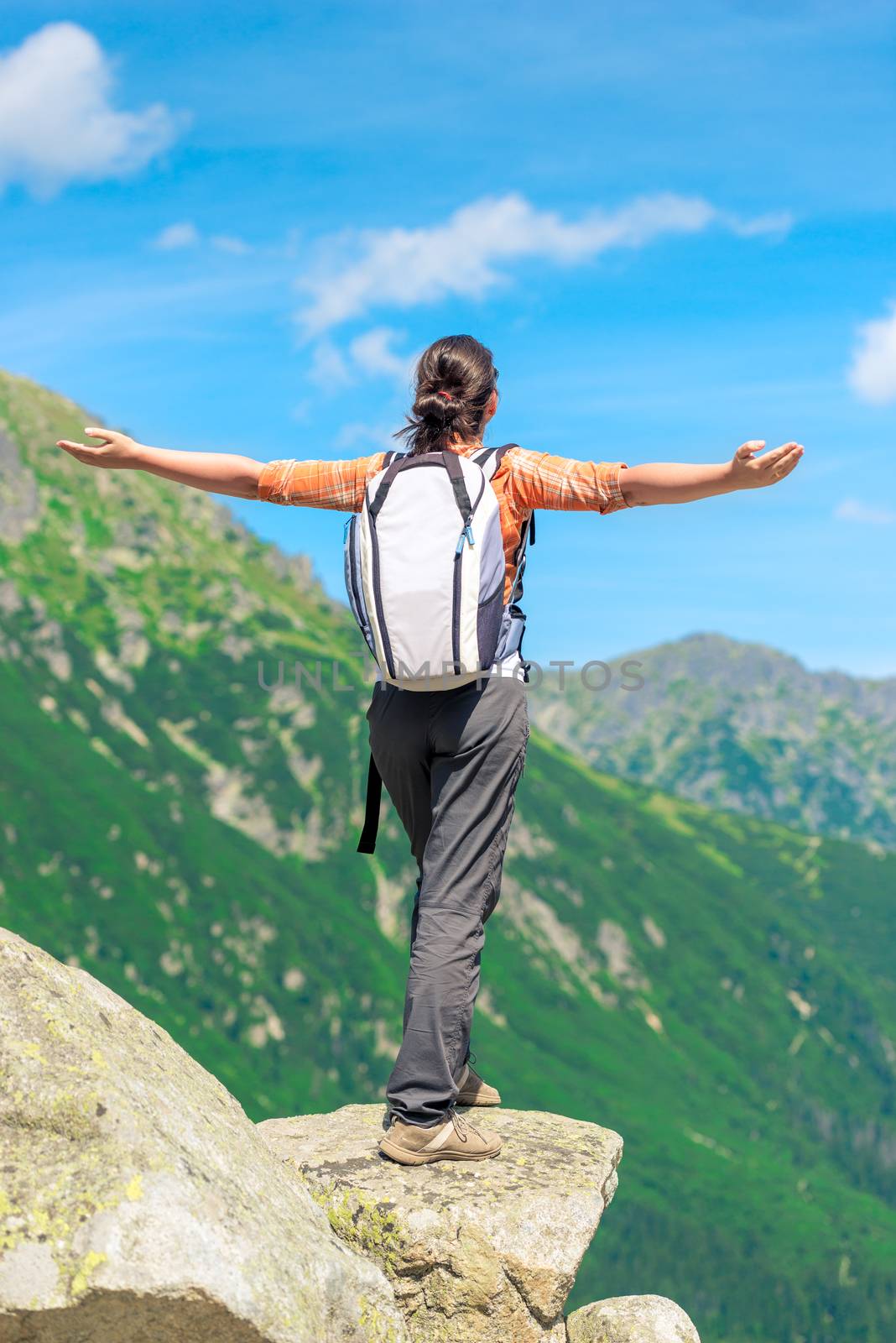 a happy tourist is standing by the cliff at the edge of the rock with arms stretched out to the side