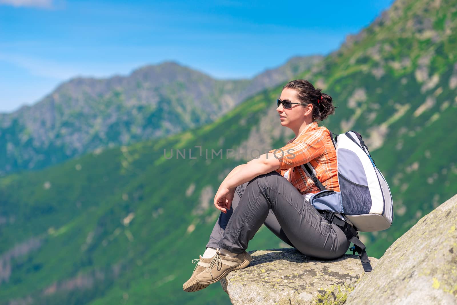 woman with a backpack resting, sitting on a stone and admiring the beautiful scenery of the mountains