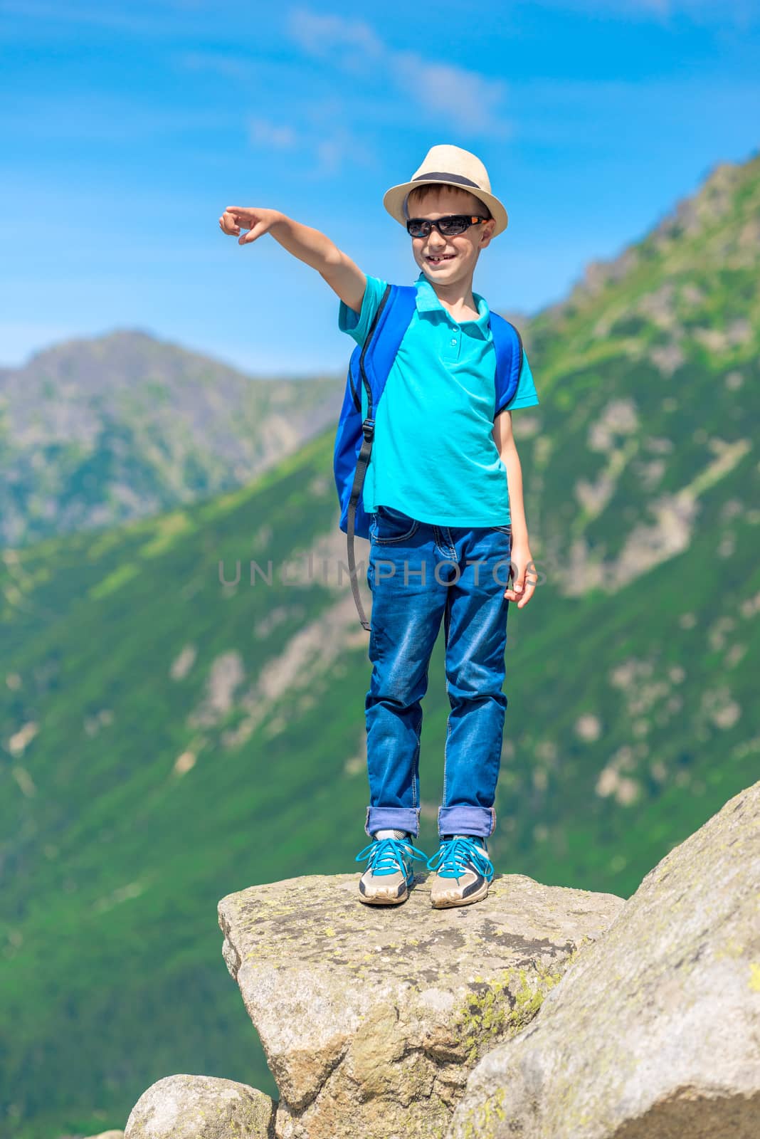 boy traveler stands on a rock and shows up a mountain by kosmsos111