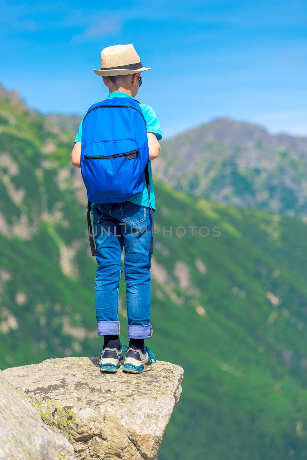 boy with a backpack in the mountains stands on a rock and looks by kosmsos111