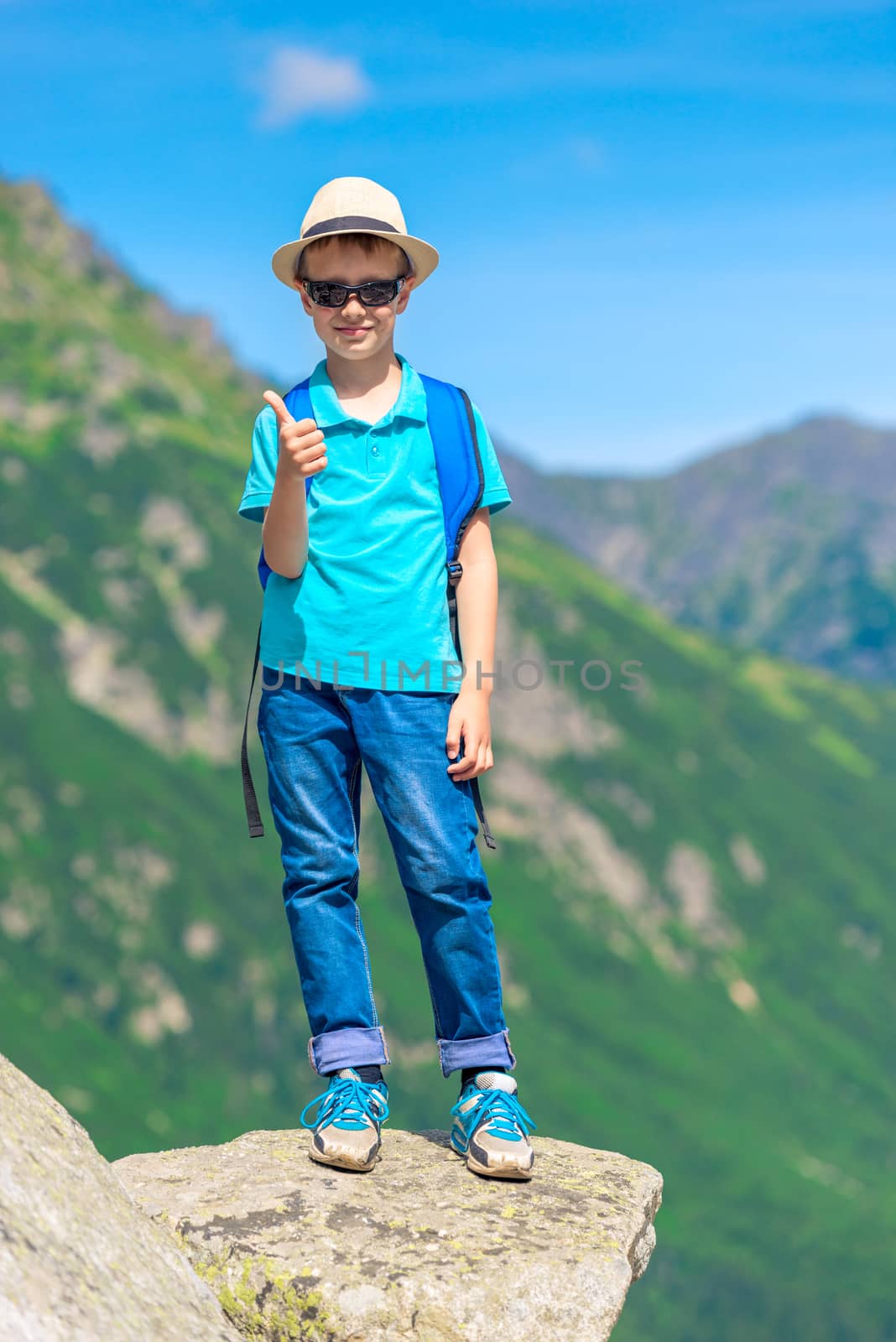 vertical portrait of a happy little traveler with a backpack on the background of mountains