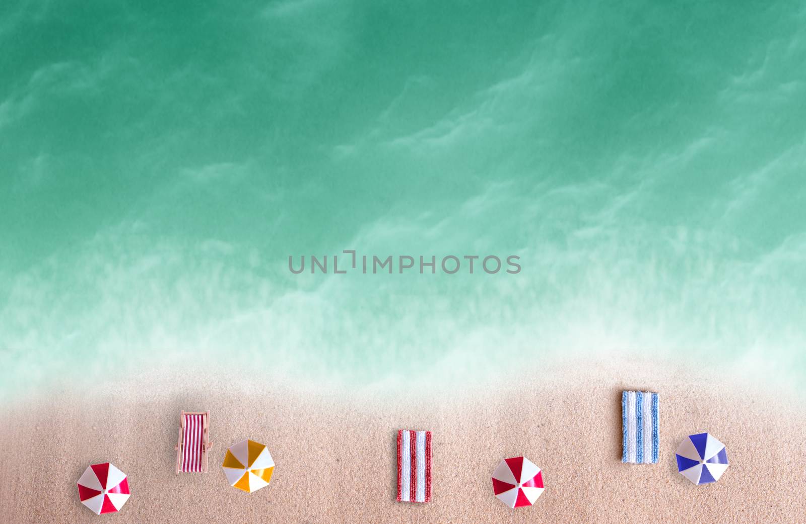 Aerial view of miniature beach parasols and towels by the sea