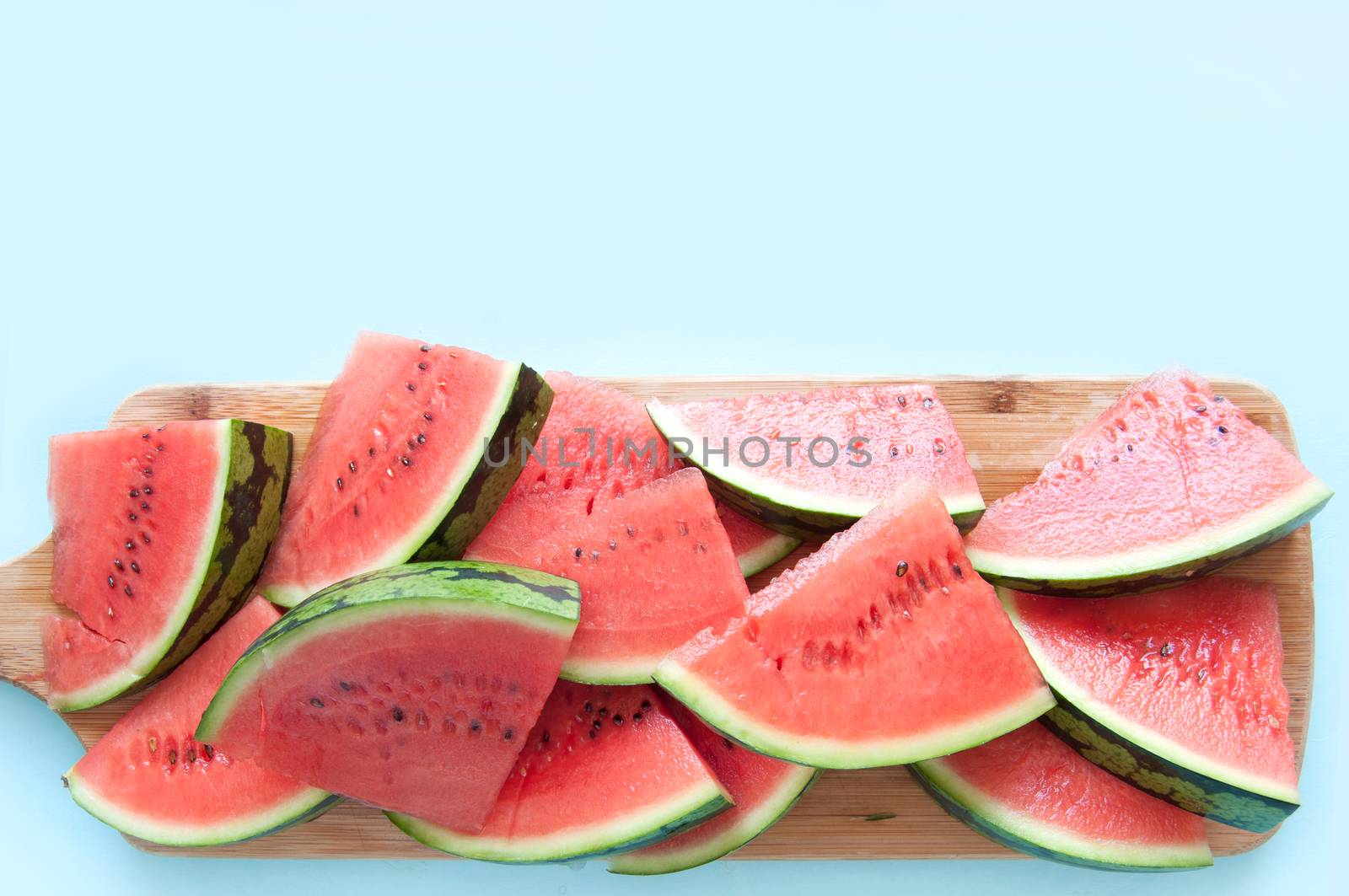 Fresh watermelon slices on chopping board over a blue background