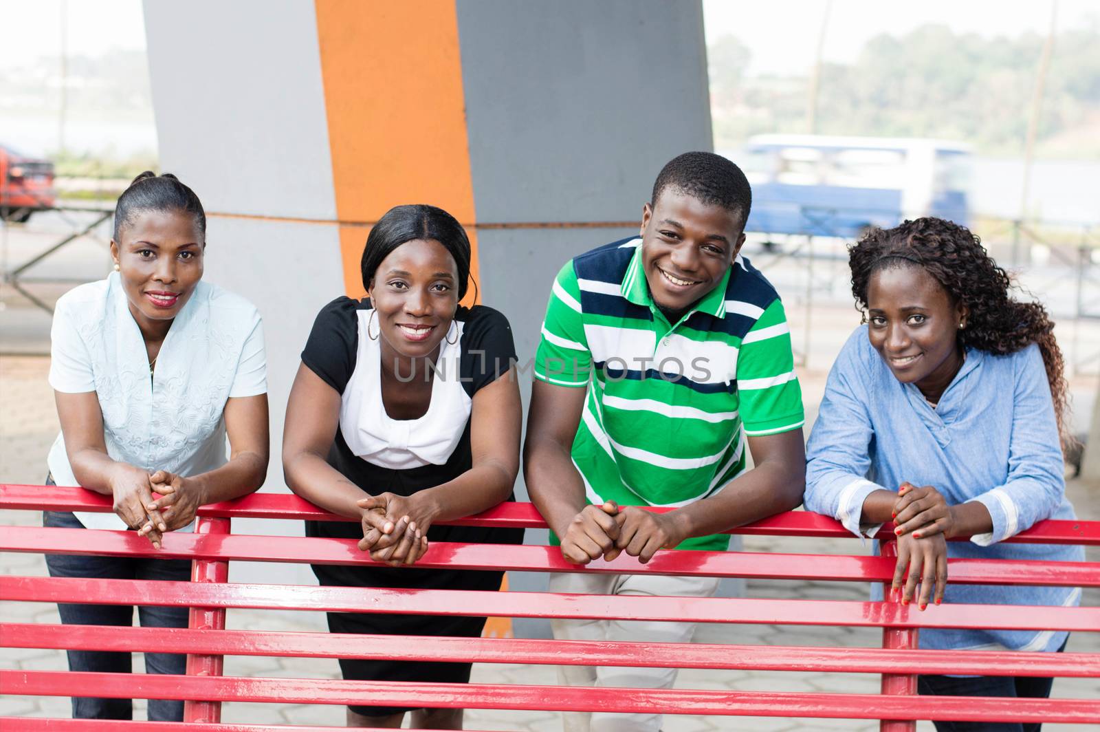 This group of young friends in a park leaning on a bench with a beautiful smile.