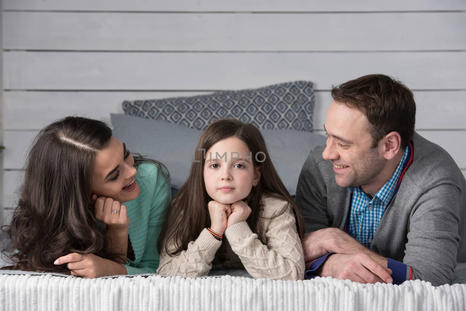 Family portrait of happy parents and their daughter laying on bed at home