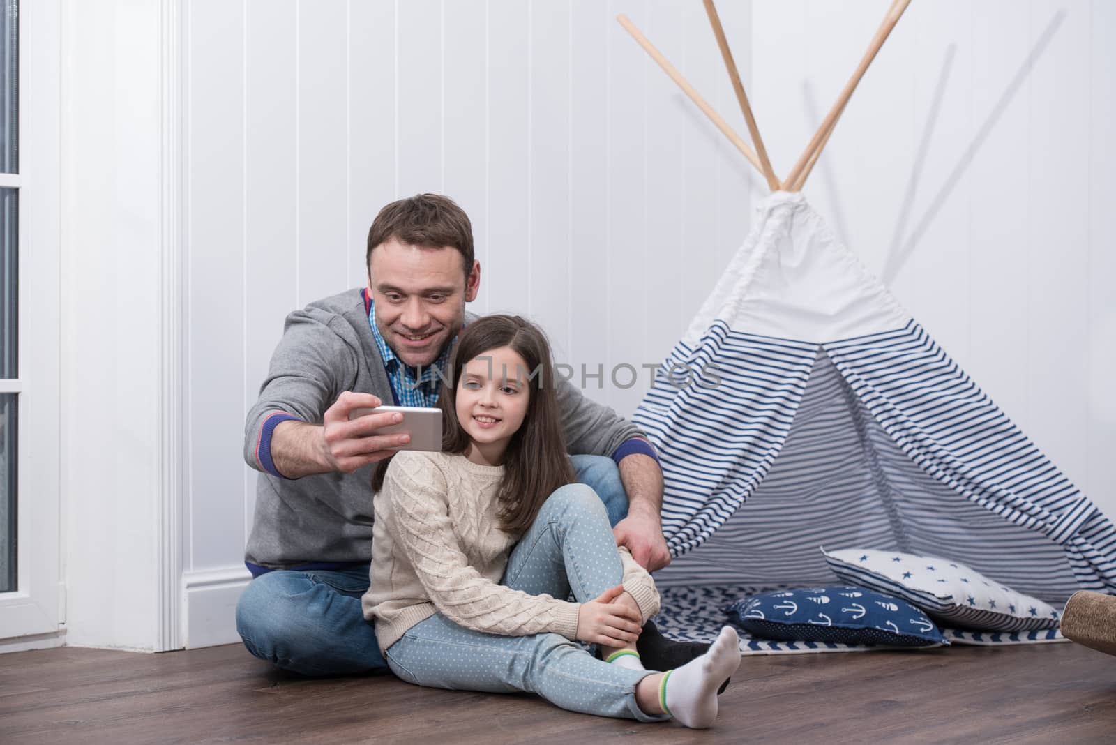 Father and daughter taking selfie playing at home with constructed wigwam