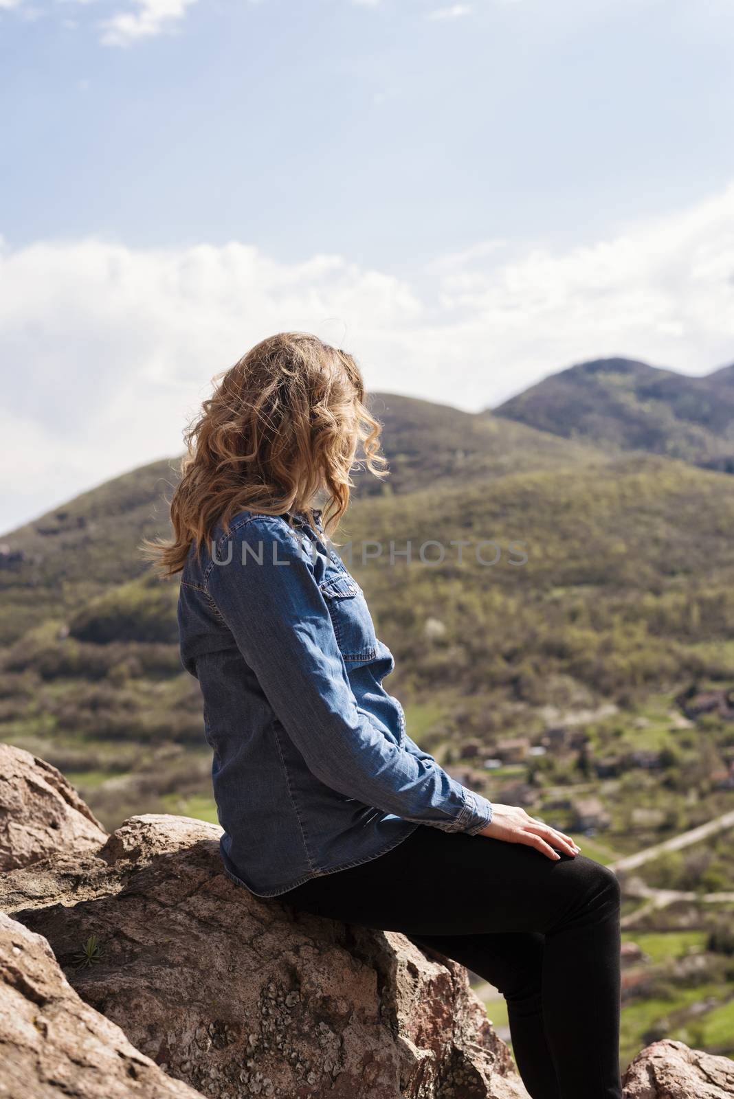 A hiking girl sits on the edge of the cliff and looking at the  valley and mountains.