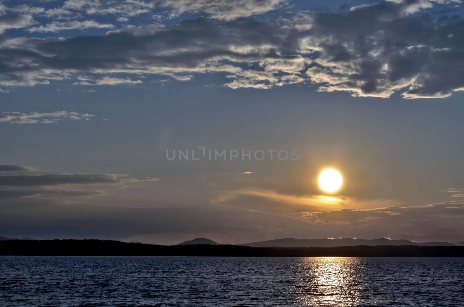 the evening sky over the lake, silhouettes of clouds illuminated by the sun, the sun sets over the horizon