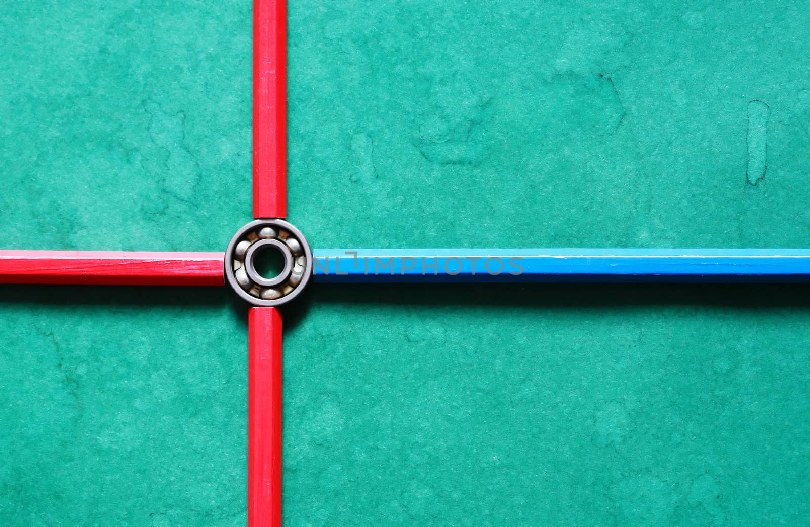 One ball bearing inside cross made from pencils on green background