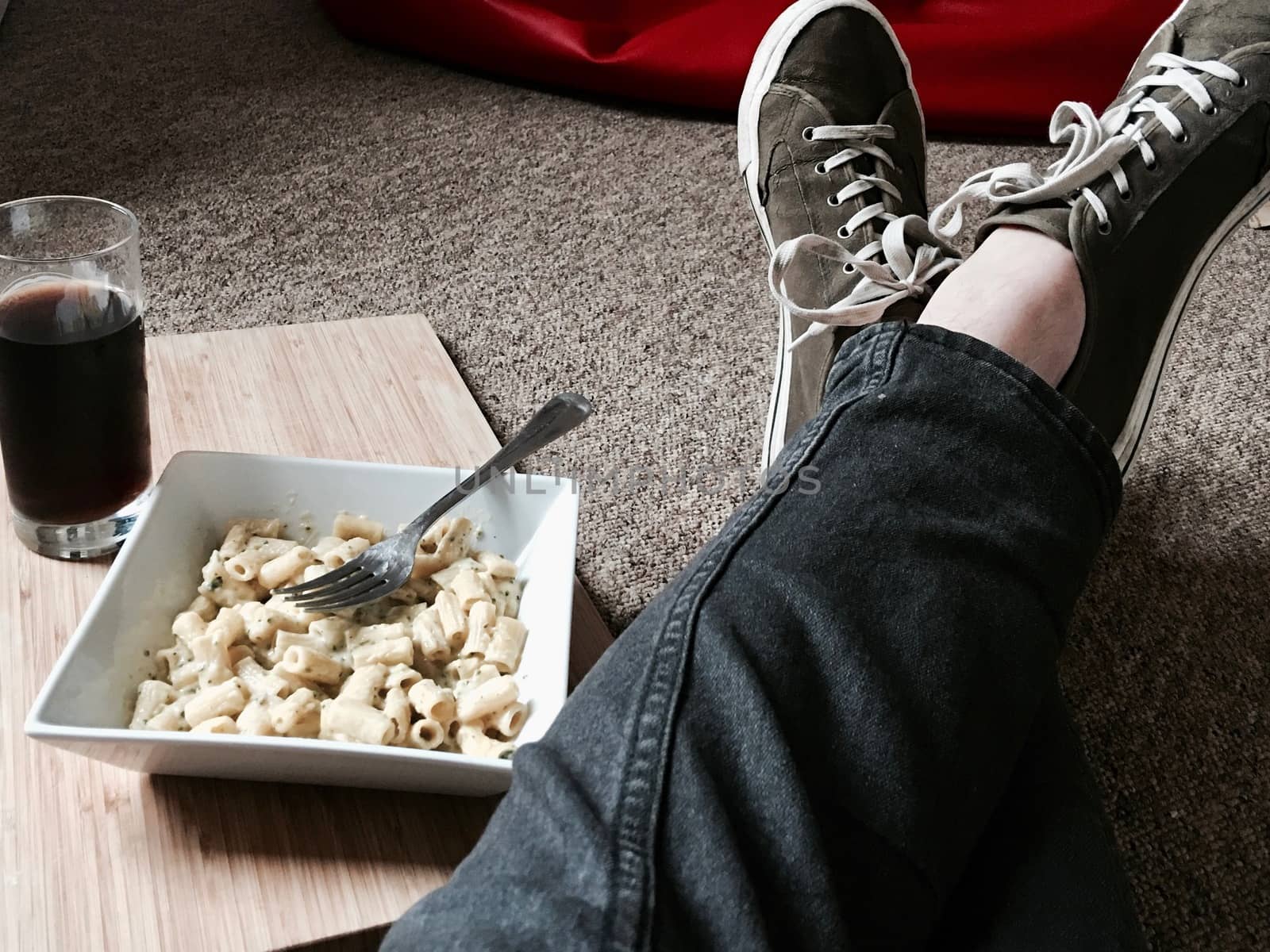 Tasty and fresh pasta in square plate on the floor near legs. Student lifestyle.
