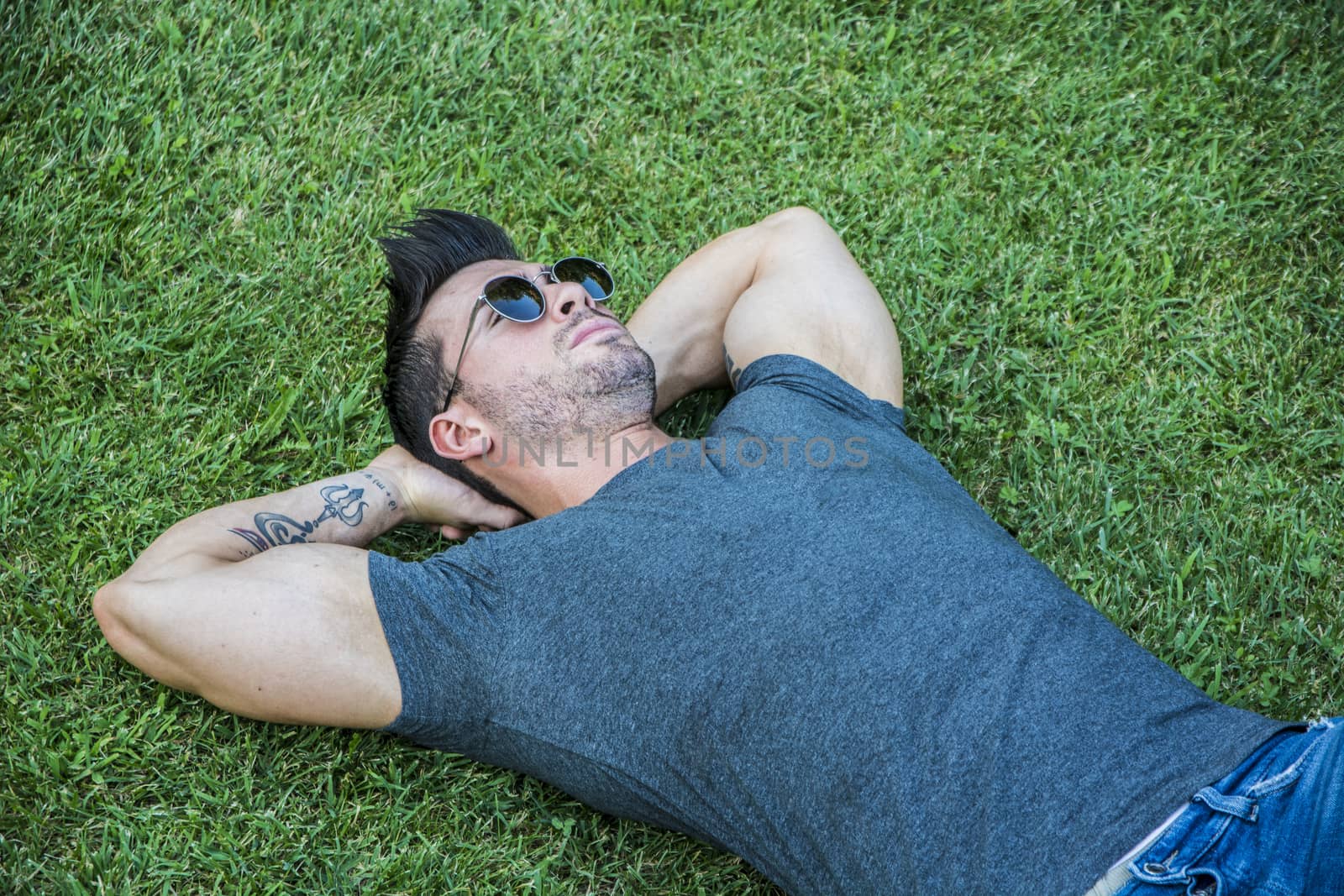 Good looking, fit male model relaxing lying on the grass, looking at camera, photographed right from above