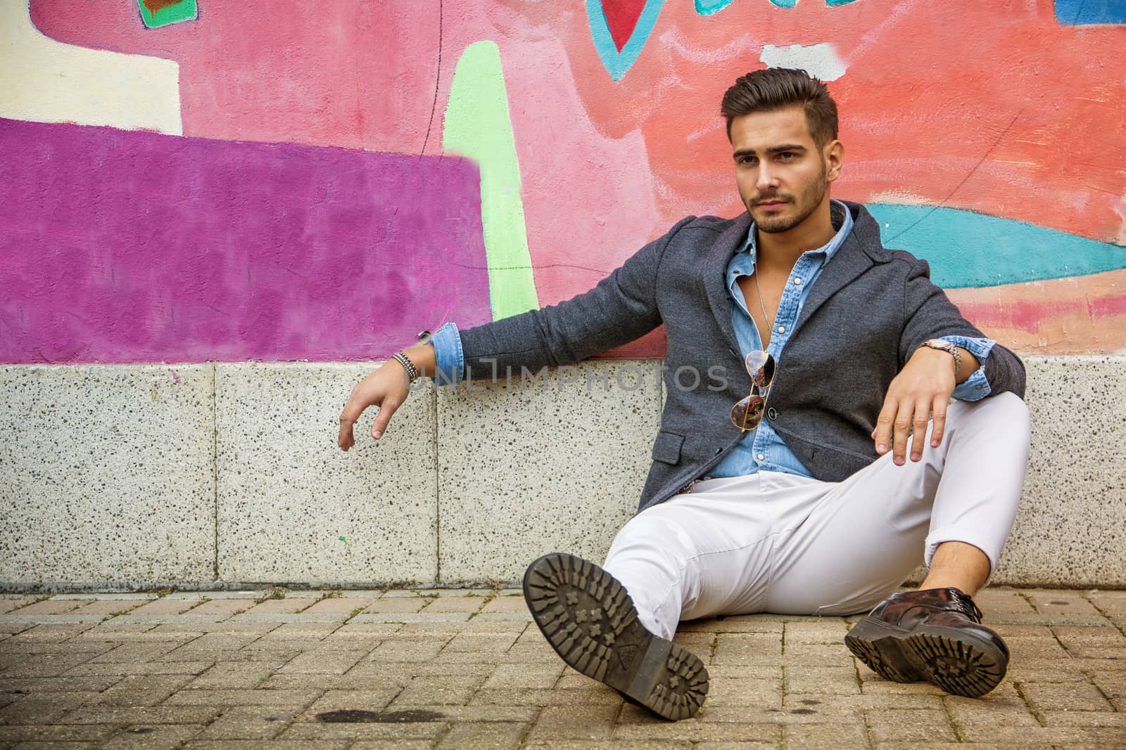 Attractive young man sitting against colorful graffiti wall, looking at camera