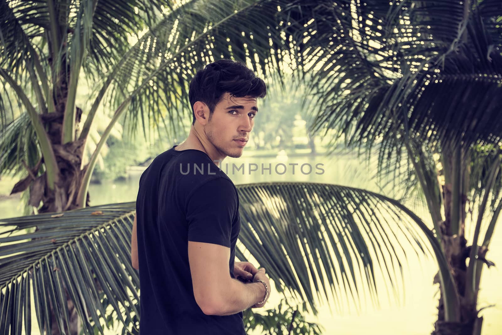 Attractive young man outdoor in nature, near palm trees in a sunny day
