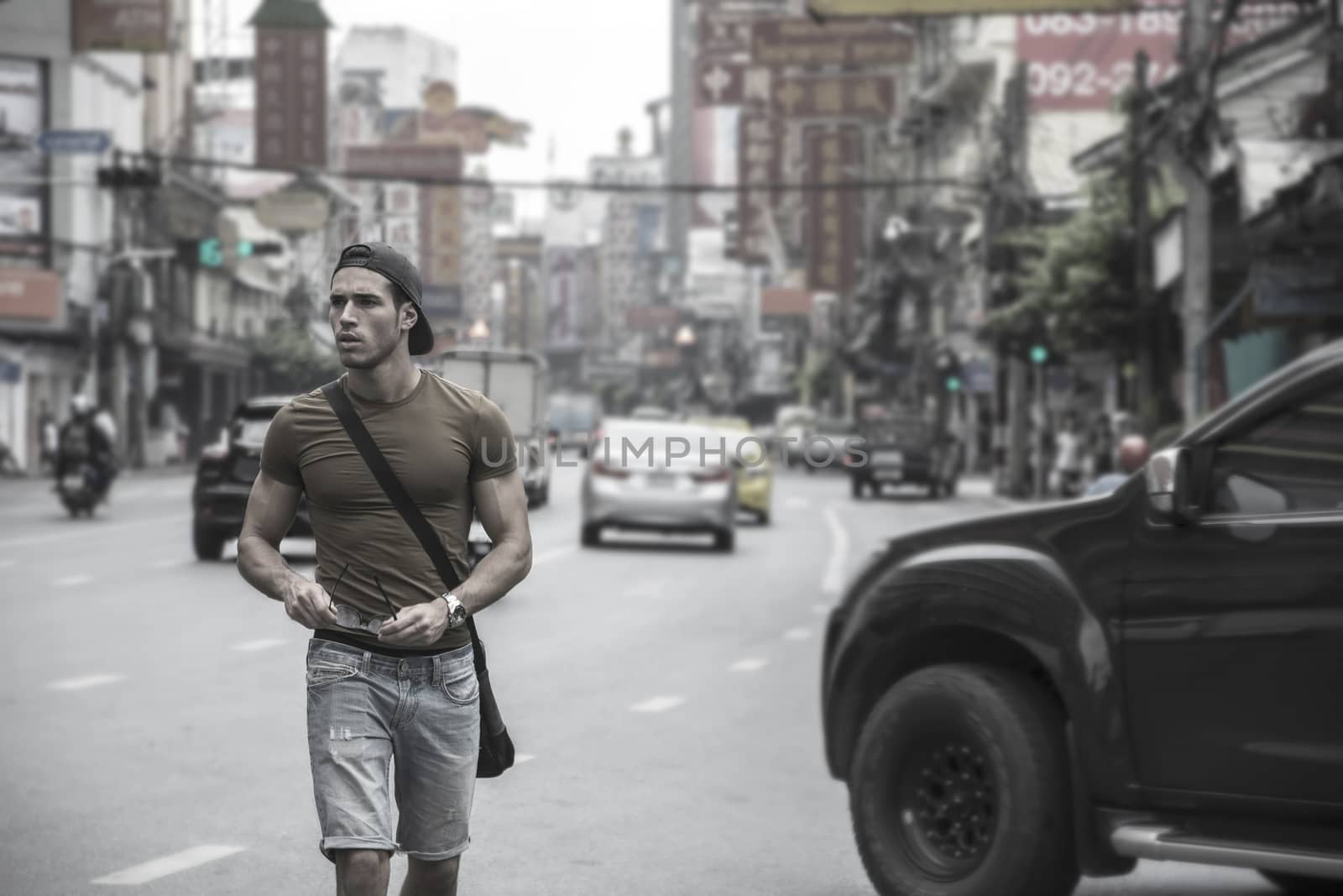 Muscular young handsome man walking on busy sunny street in Bangkok, Thailand.