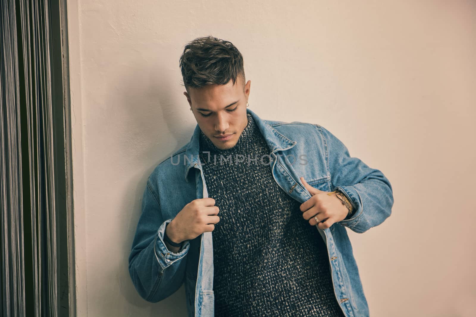 Handsome white asian young man wearing blue denim jacket, standing on light background against wall in studio shot