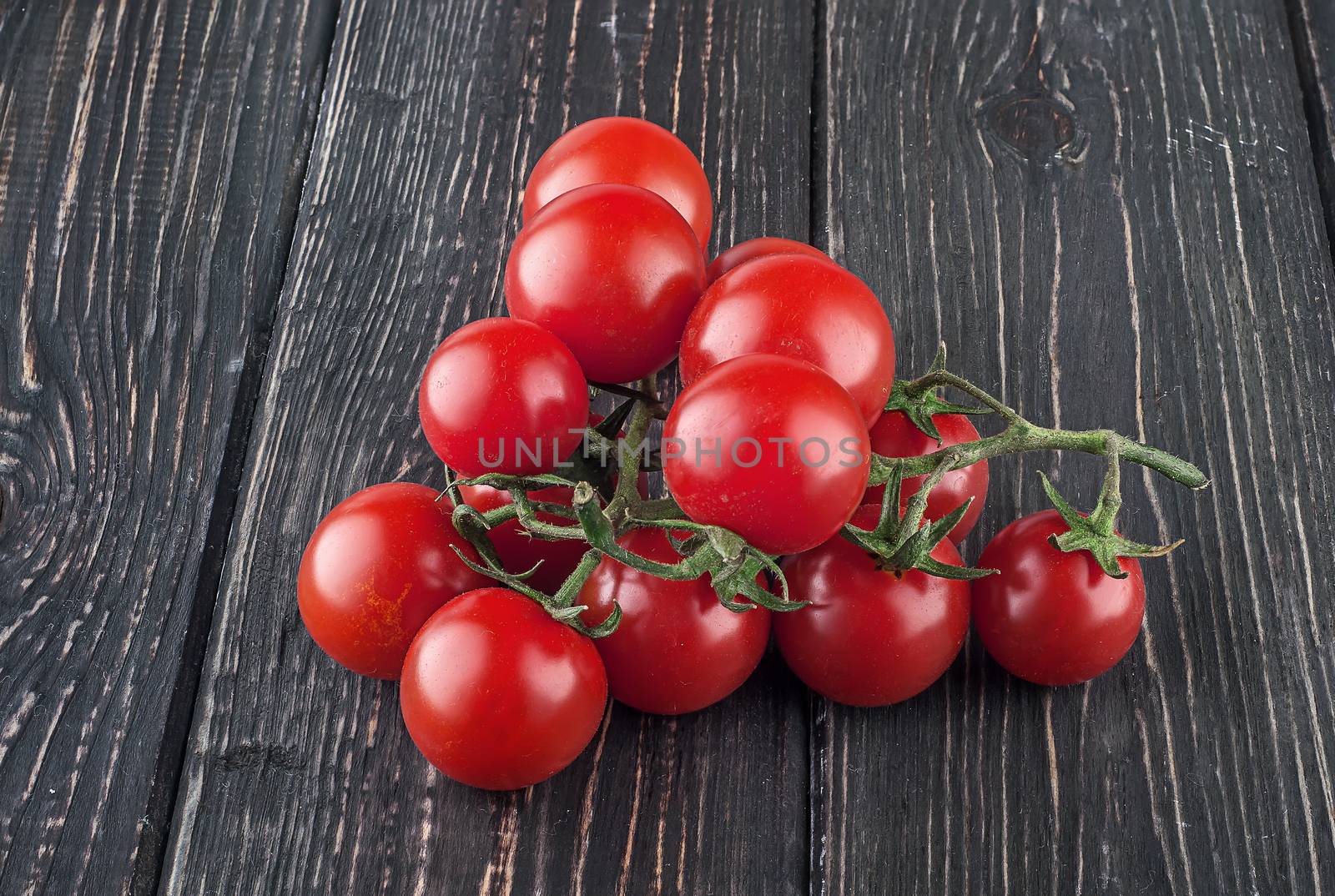 Two branches of cherry tomatoes. Dark wooden table. Blurred background.