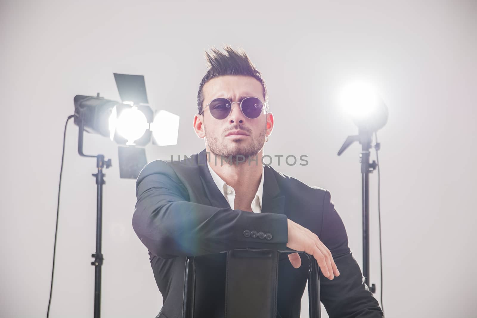 Handsome man in stylish suit and sunglasses posing in studio lights.