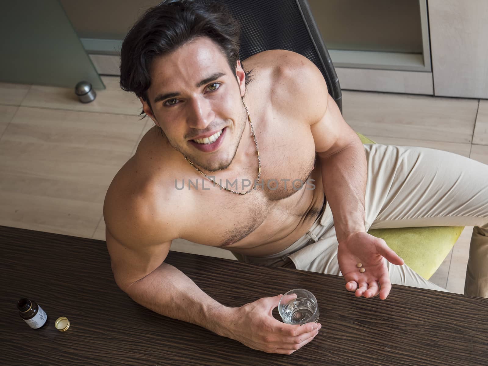 From above shot of happy muscular shirtless man sitting on chair taking pills smiling at camera