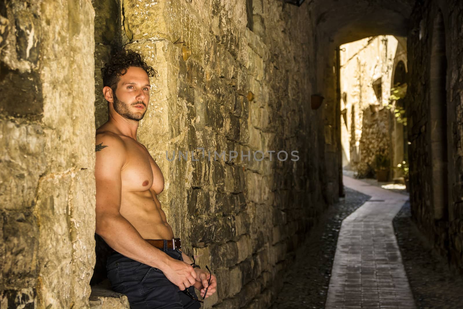 Handsome muscular shirtless man walking on old brick lane. Horizontal outdoors shot