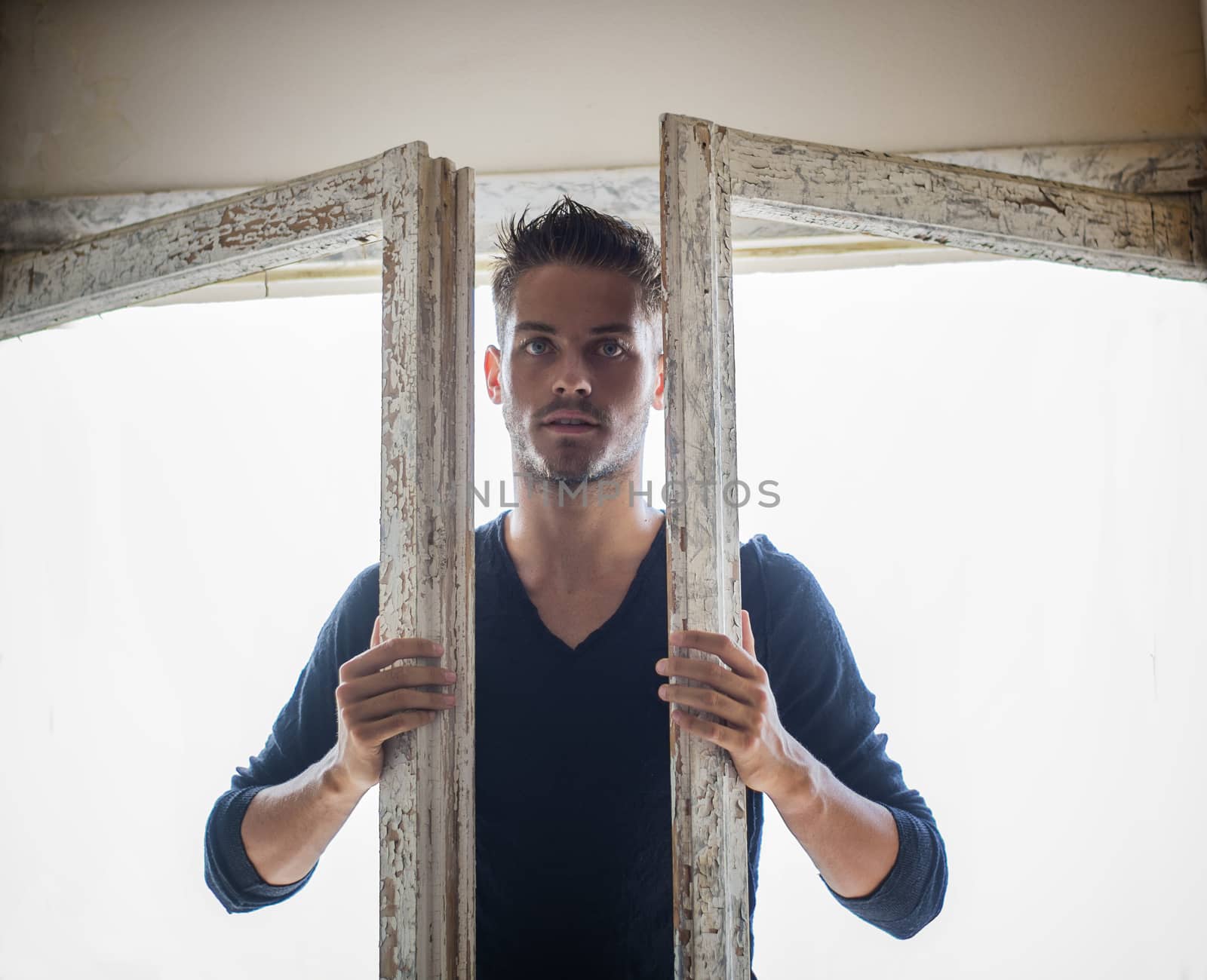 Portrait of handsome young man with beard entering the room with wooden doors